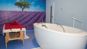 Ein Zimmer mit einer großen Badewanne, einem Massagetisch mit roher Decke und einem Wandgemälde, das ein Lavendelfeld zeigt.
