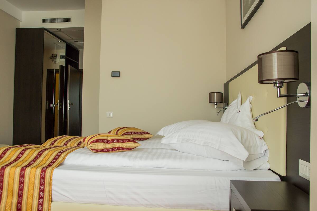 A hotel room with a bed, a bedside table, a lamp, and a mirror on the wall.