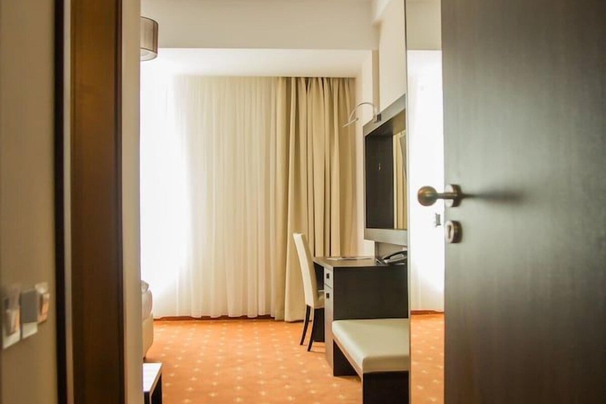 A hotel room with a bed, a desk, a chair, a television, and a window with curtains.