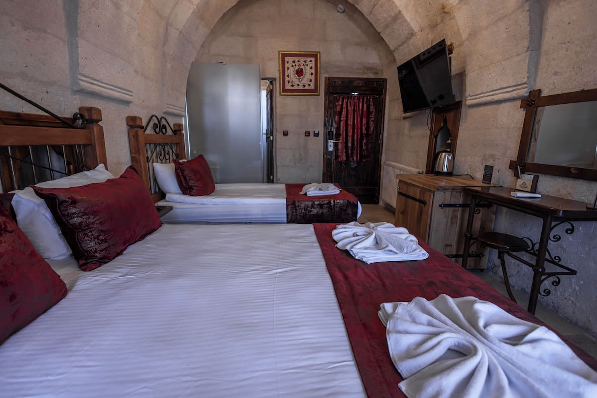 Une chambre d’hôtel avec deux lits, un bureau en bois, une télévision et un rideau rouge.