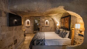 A stone-walled bedroom with a bed, a flat-screen TV, and a wooden headboard. - Göreme Cave Suites (Nevsehir)