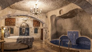 A historic room with a large bed, a stone wall, a fountain, and a chandelier. - Göreme Cave Suites (Nevsehir)