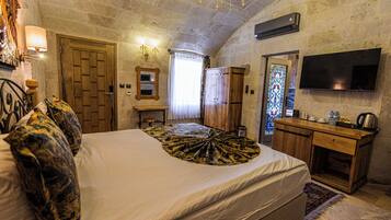 A bedroom with a large bed, a wooden desk, a television, and a stone wall.