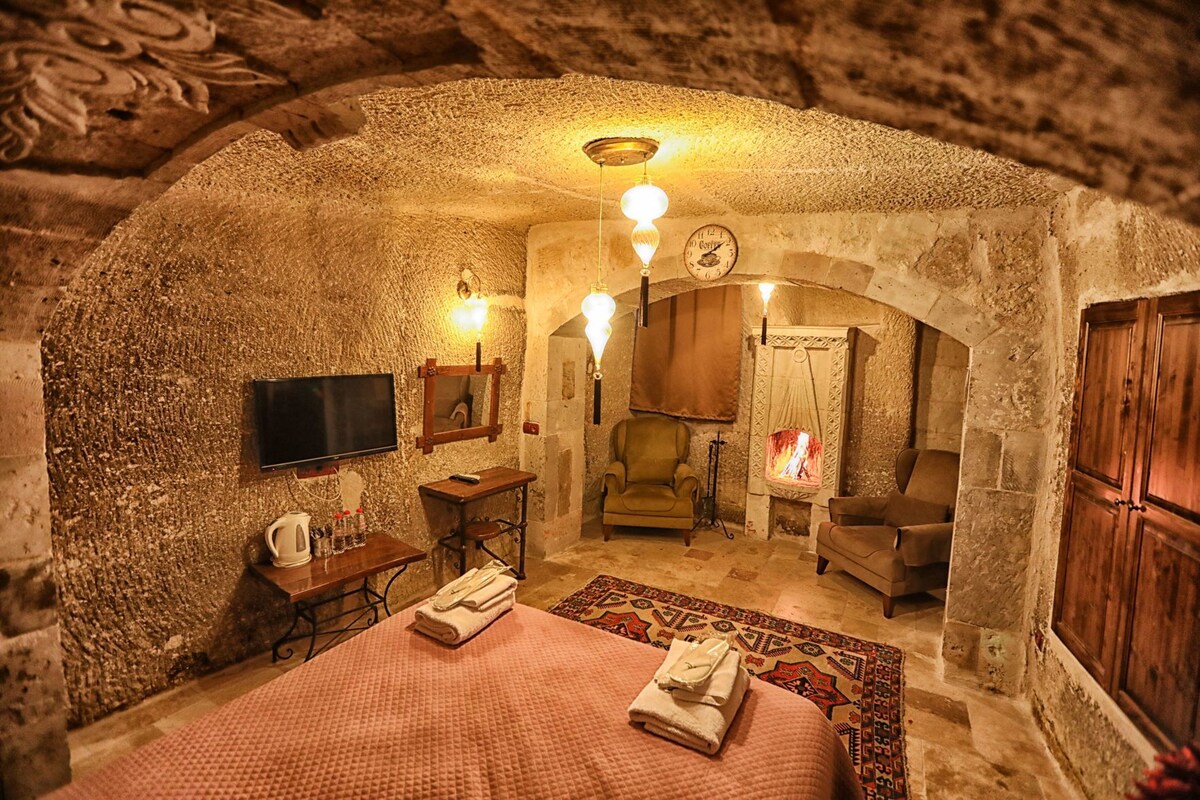 A stone-walled room with a bed, a chair, a television, and a fireplace.