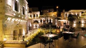 An outdoor dining area with tables and chairs, a staircase, and a building facade with lights. - Göreme Cave Suites (Nevsehir)