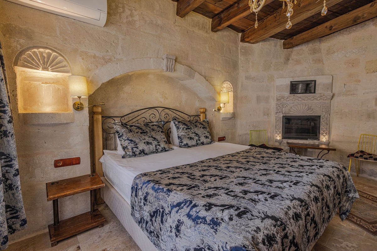 Une chambre avec un grand lit, des murs en pierre, une cheminée et deux lampes fixées au mur.