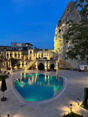 A pool area with a stone building and a large rock formation. - Göreme Cave Suites (Nevsehir)