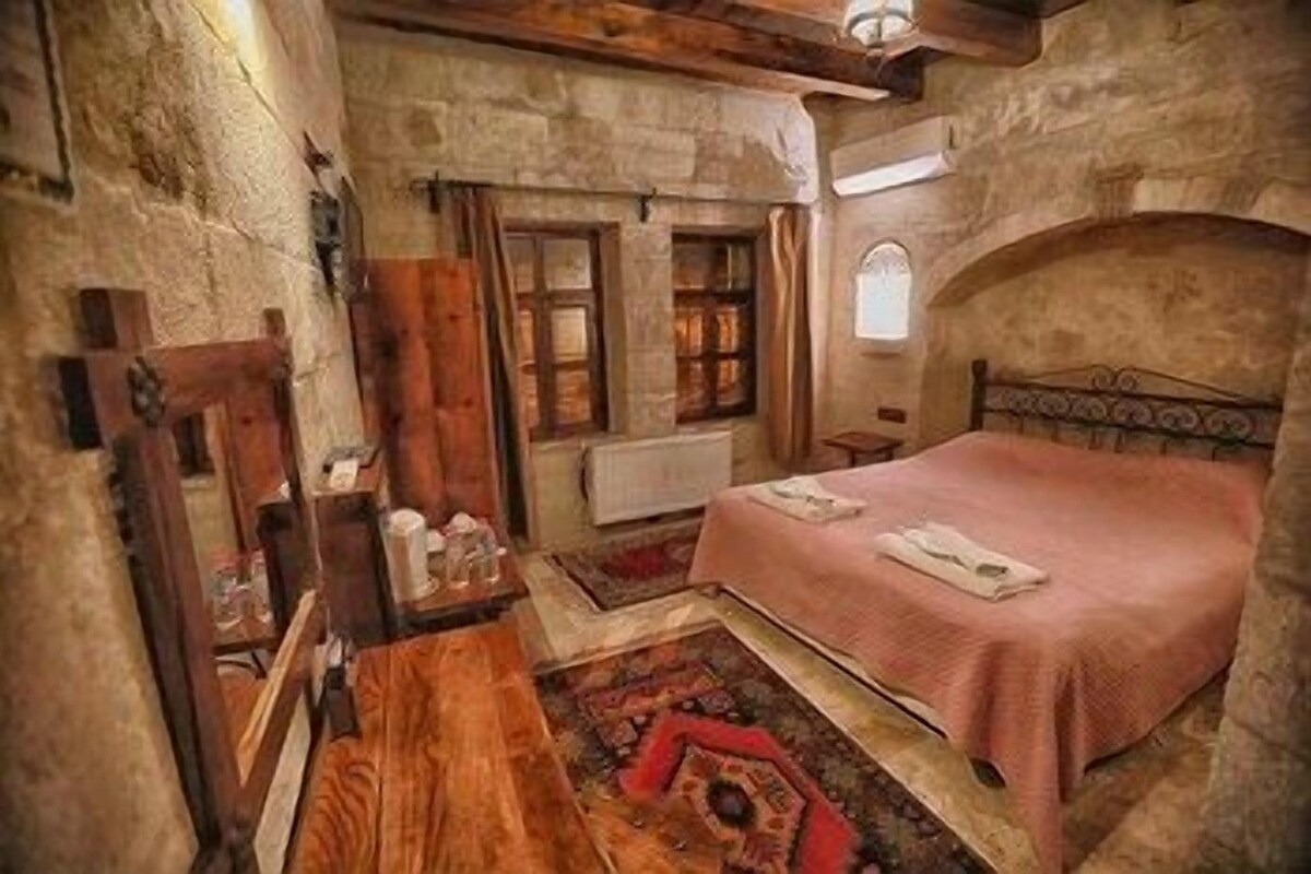 A bedroom with a stone wall, a wooden bed, a small table, and a window.