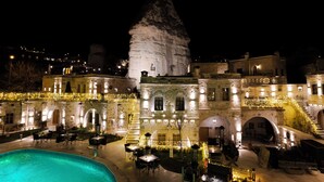 A historic building with a prominent conical tower, outdoor seating area with tables and chairs, and a swimming pool. - Göreme Cave Suites (Nevsehir)