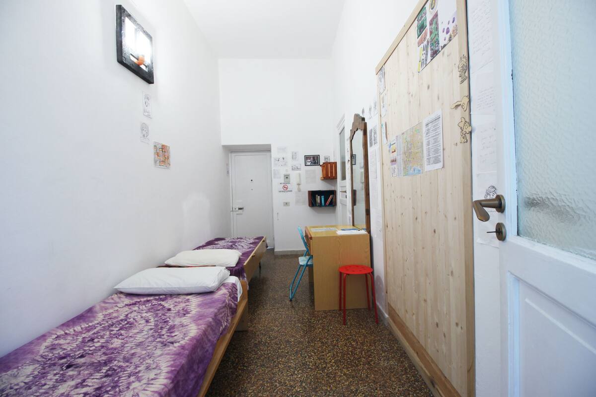 A dormitory room with three single beds, a desk, a chair, and a door with a bulletin board.