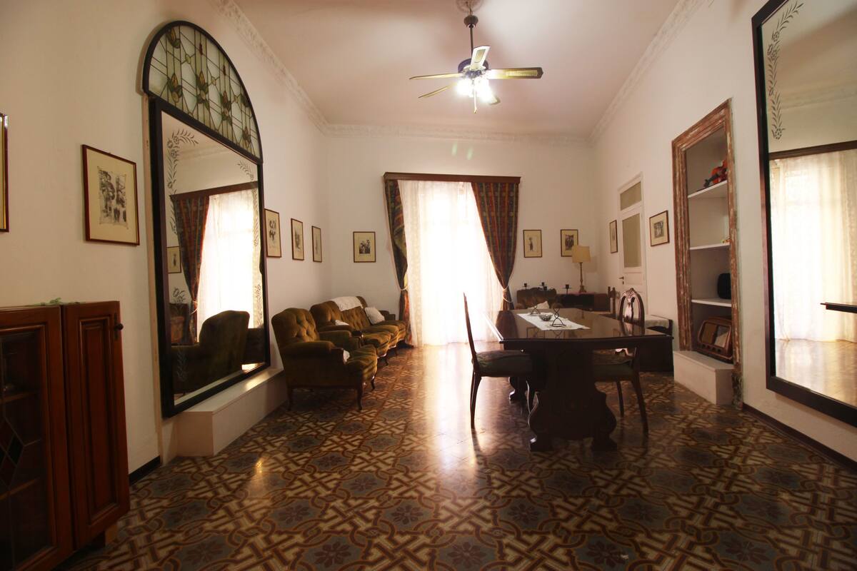 A room with patterned flooring, a ceiling fan, a dining table with chairs, a sofa, and a large mirror.