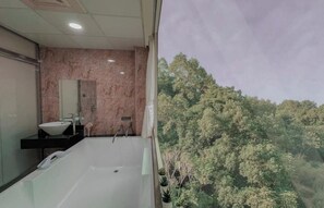 A bathroom with a large bathtub, a sink, and a mirror. There is a view of trees outside the window.