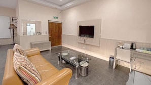 A modern lobby with a leather sofa, a glass coffee table, a TV mounted on the wall, and a kitchenette area. - Ruixiong Hotspring Villa (Ruisui)