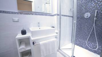 Een moderne badkamer met een douchecabine van glas, een wit wastafeltje en een betegelde spatwand.