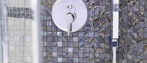 A shower with a chrome faucet and a glass door, set against a mosaic tile wall.