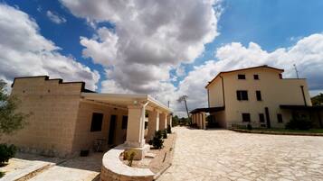 A courtyard with stone flooring, a covered seating area, and a building with a flat roof.