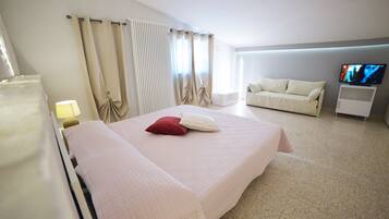 Una habitación de hotel con una cama grande, un televisor sobre un mueble bajo y un sofá.