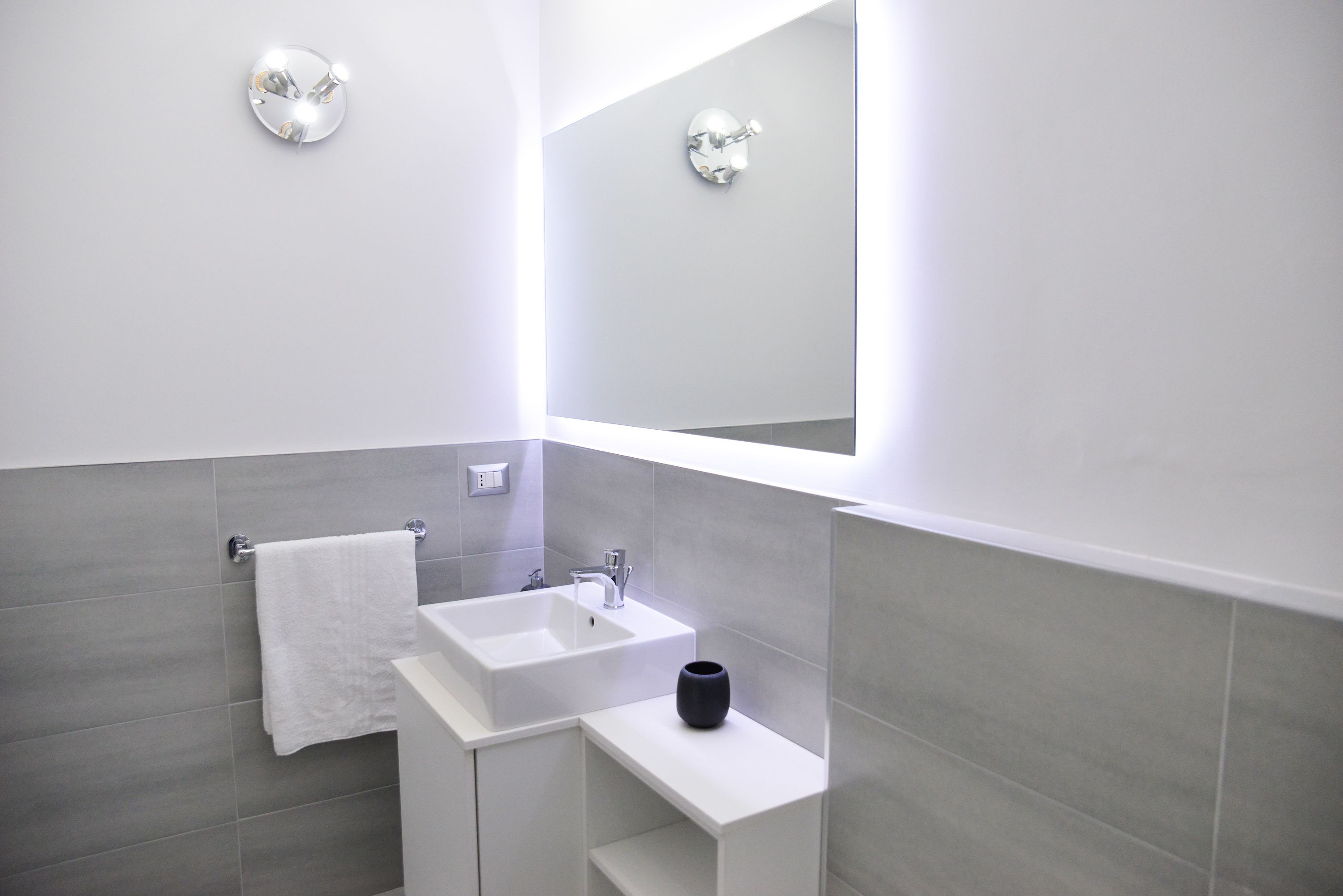 A modern bathroom with a white sink, a black vase, and a towel hanging on the wall.