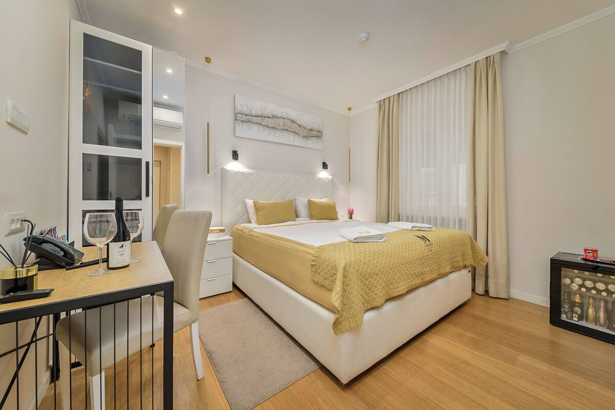 Una habitación de hotel moderna con una cama grande, mesitas de noche, un escritorio con teléfono y gafas, y un minibar.