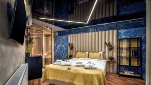 A modern hotel room with a large bed, a flat-screen TV, a minibar, and a marble-patterned wall. - Boutique Hotel Madison (Zagreb)