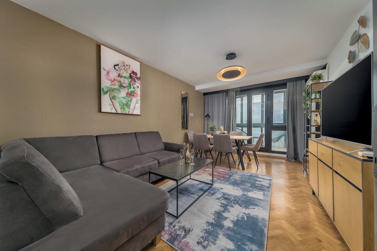 Una sala de estar moderna con un sofá seccional gris, una mesa de centro de vidrio y un comedor con mesa y sillas.