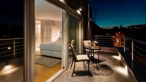 A balcony with a bed, a table with chairs, and a view of the city at night. - Boutique Hotel Madison (Zagreb)
