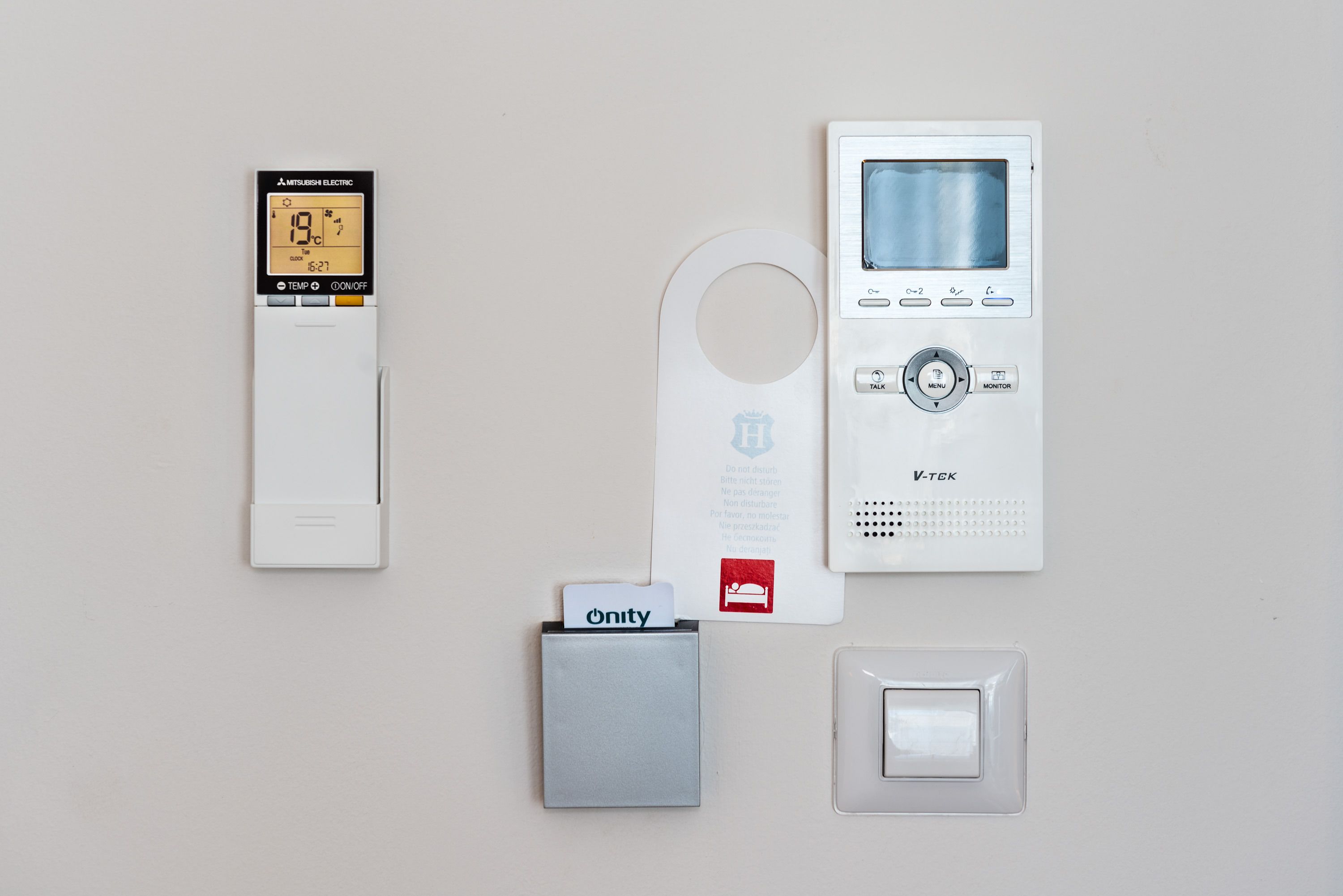 Ein Thermostat, eine Gegensprechanlage, ein Briefkasten und ein Lichtschalter an einer Wand.