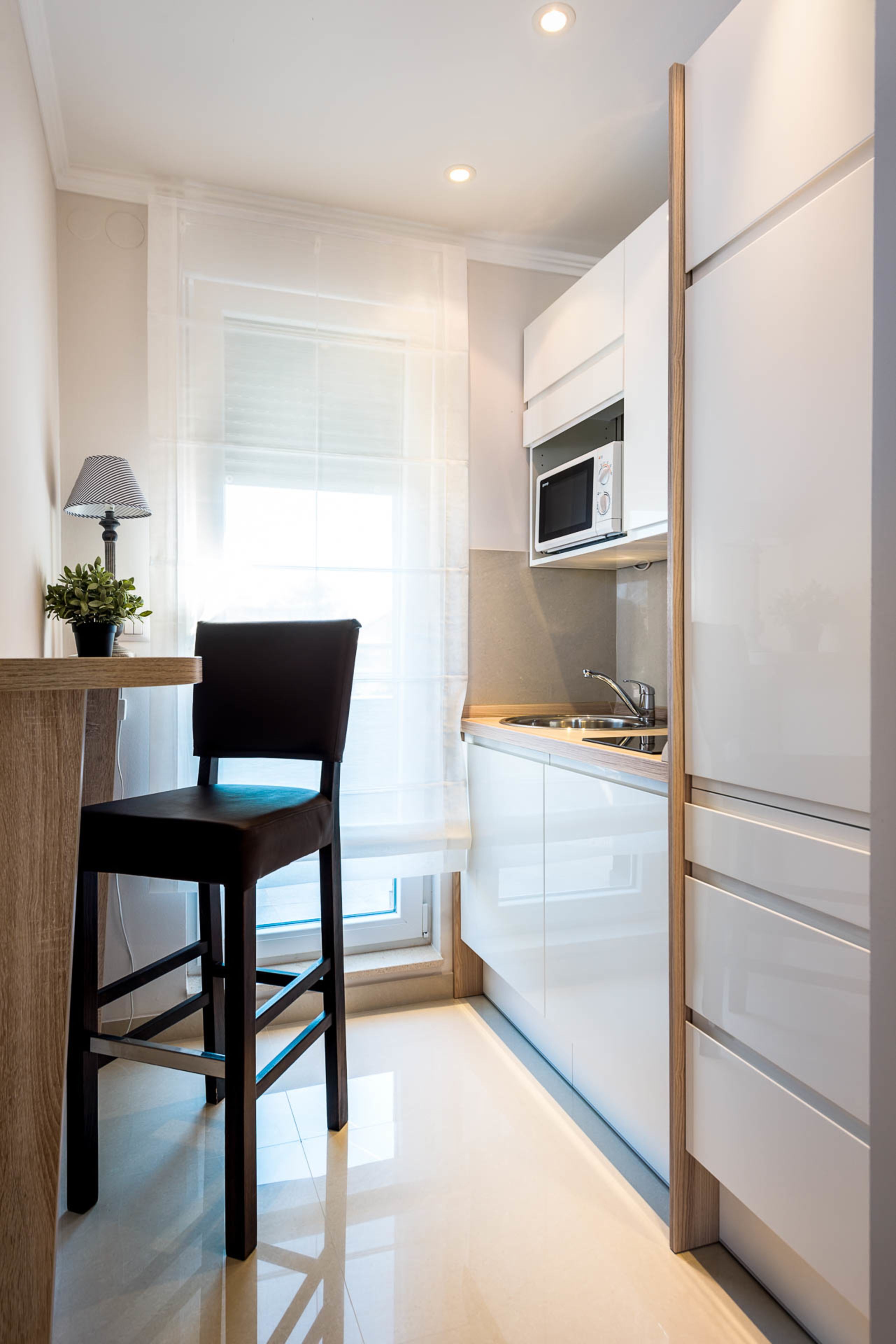 Una cocina moderna con armarios blancos, un microondas, un fregadero y una silla.