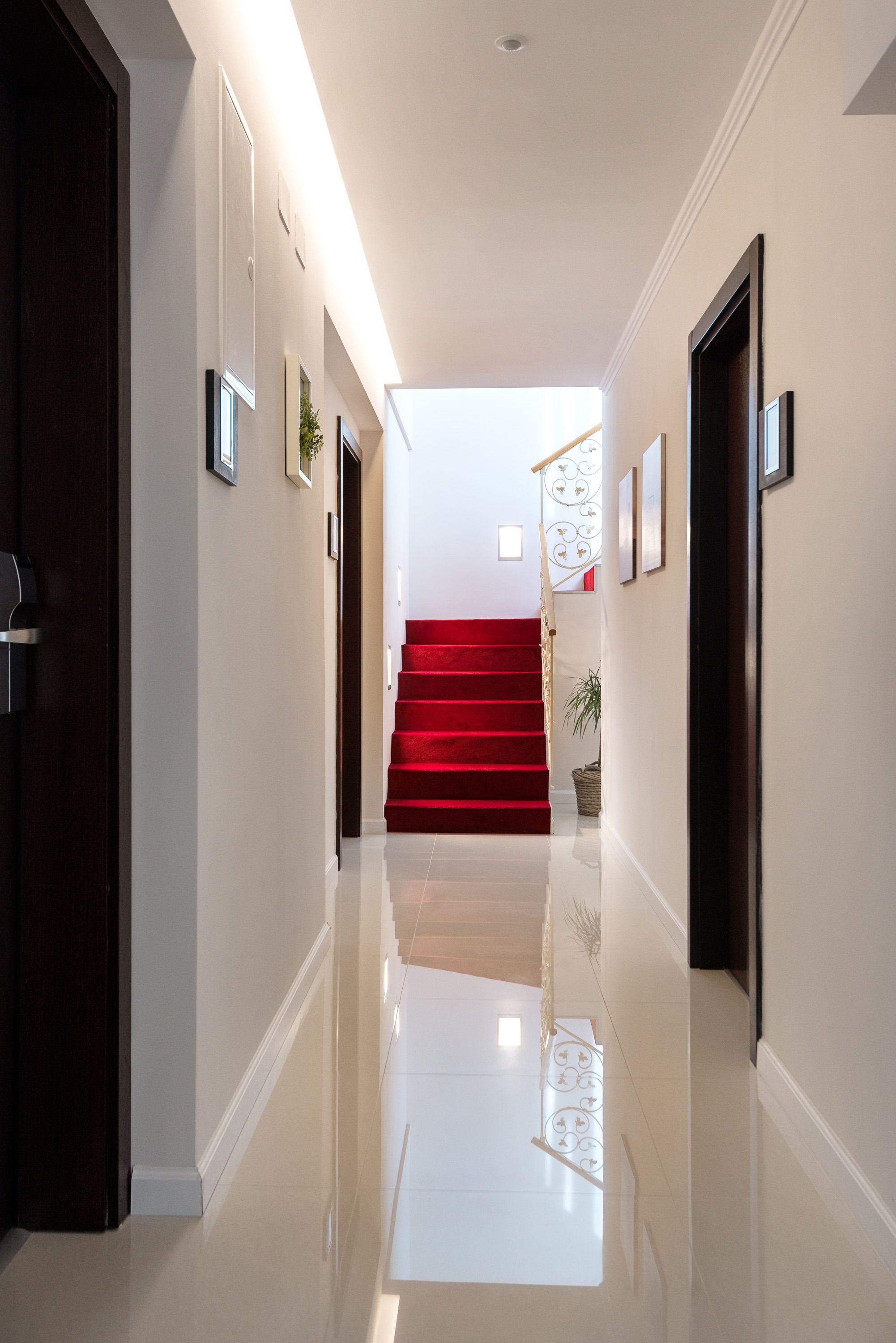 A hallway with a polished floor, a red carpeted staircase, and framed pictures on the walls.