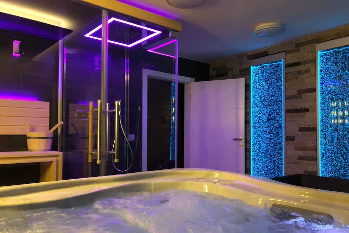 Un baño moderno con jacuzzi, cabina de ducha de vidrio e iluminación LED azul.