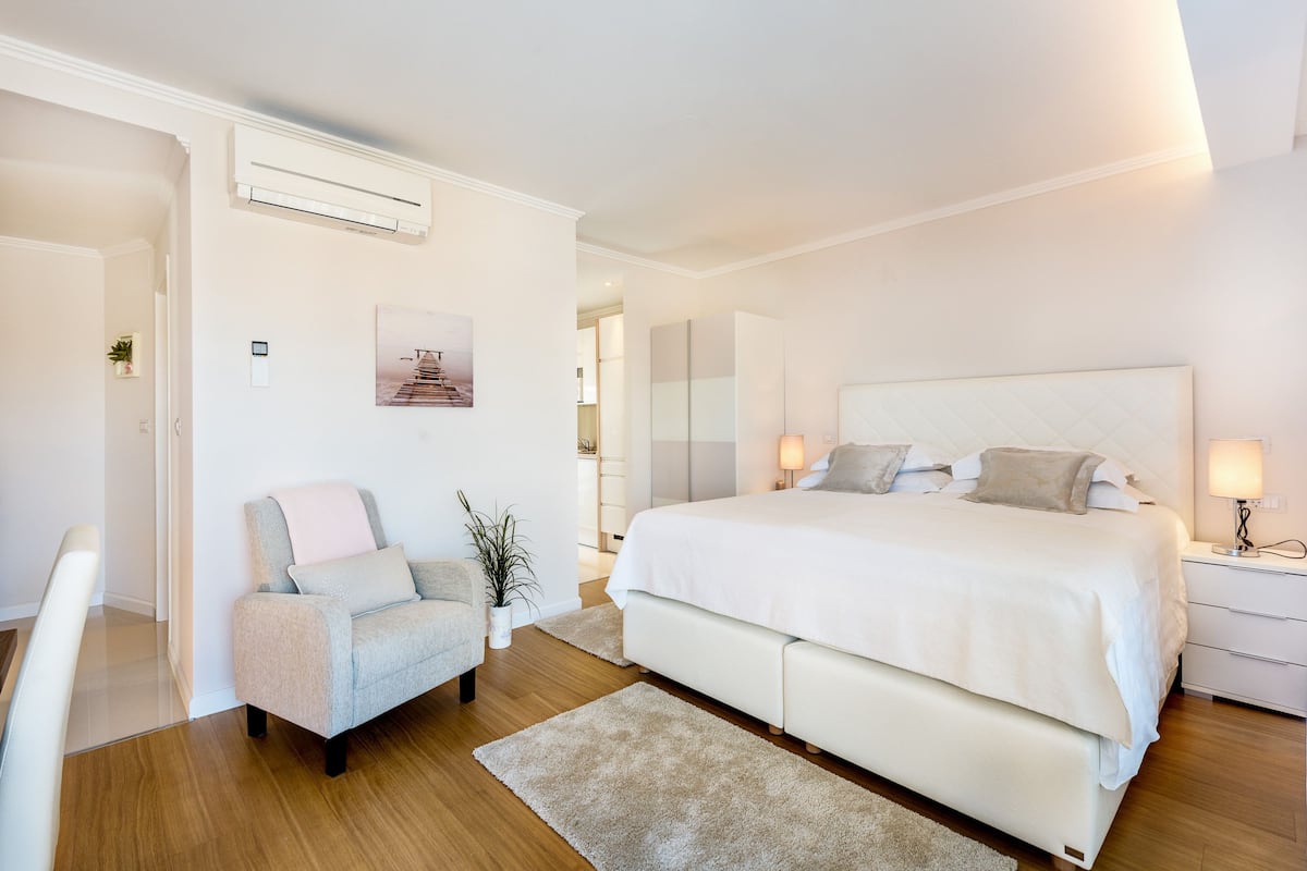 Un dormitorio moderno con una cama grande, una silla, una mesita de noche y un equipo de aire acondicionado.