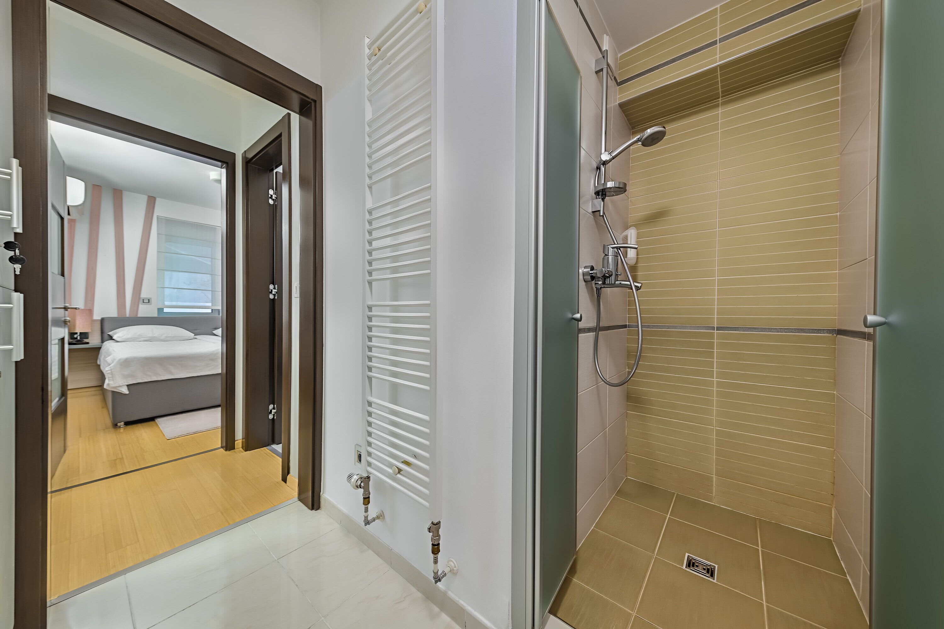 Uma casa de banho moderna com chuveiro, sanita e bidé. É visível um porta-toalhas e uma cabine de duche em vidro.