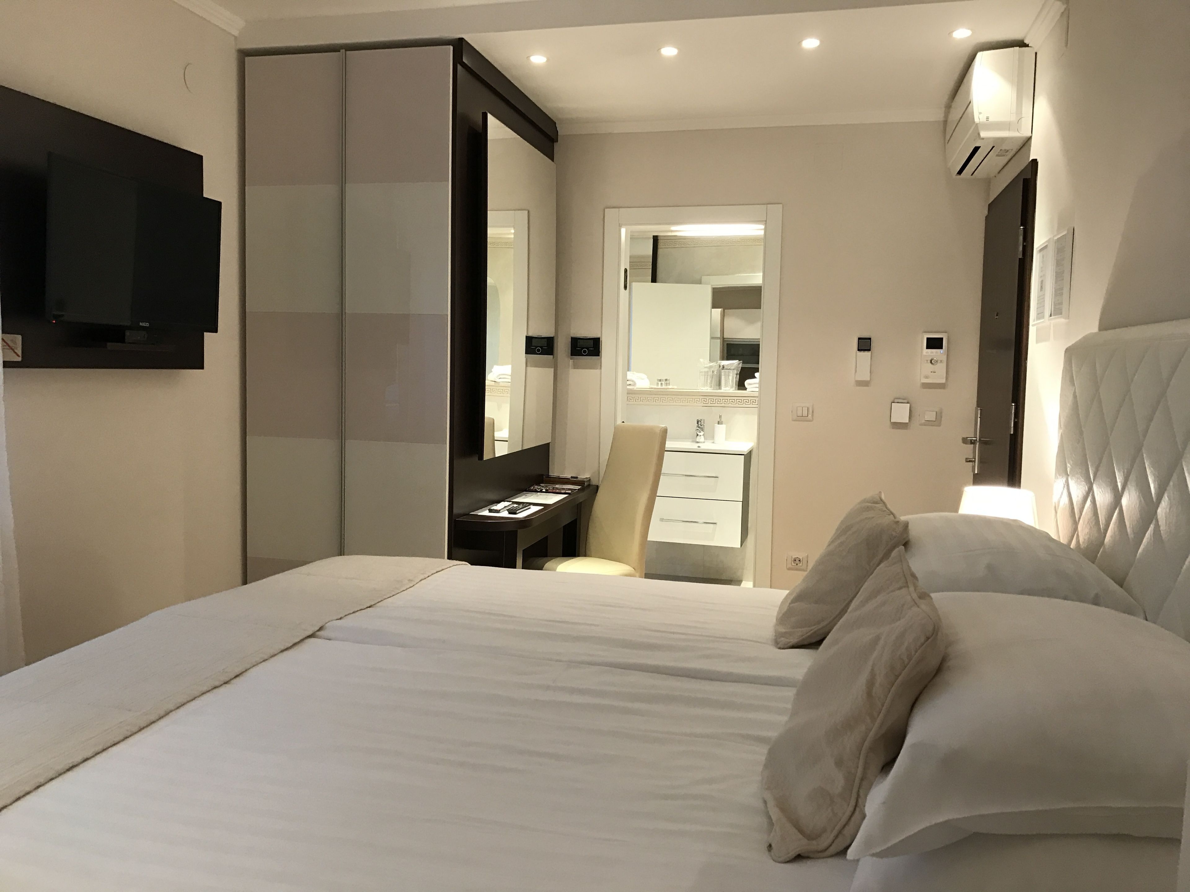 A modern hotel room with a large bed, a bedside table, a mirror, a wardrobe, and a TV mounted on the wall.