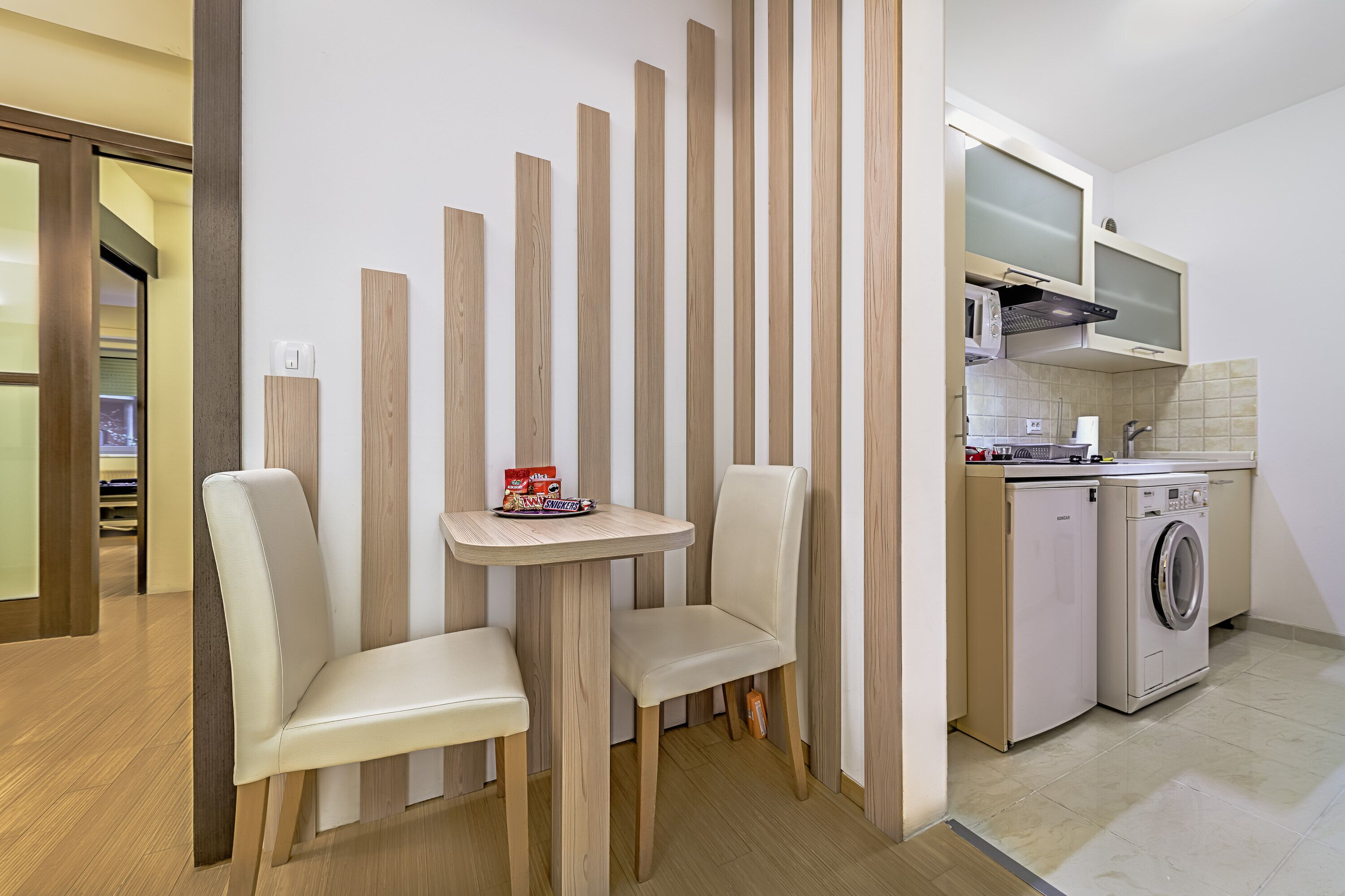 Une cuisine moderne équipée d’un lave-linge, d’une petite table avec deux chaises et d’une cloison en bois.