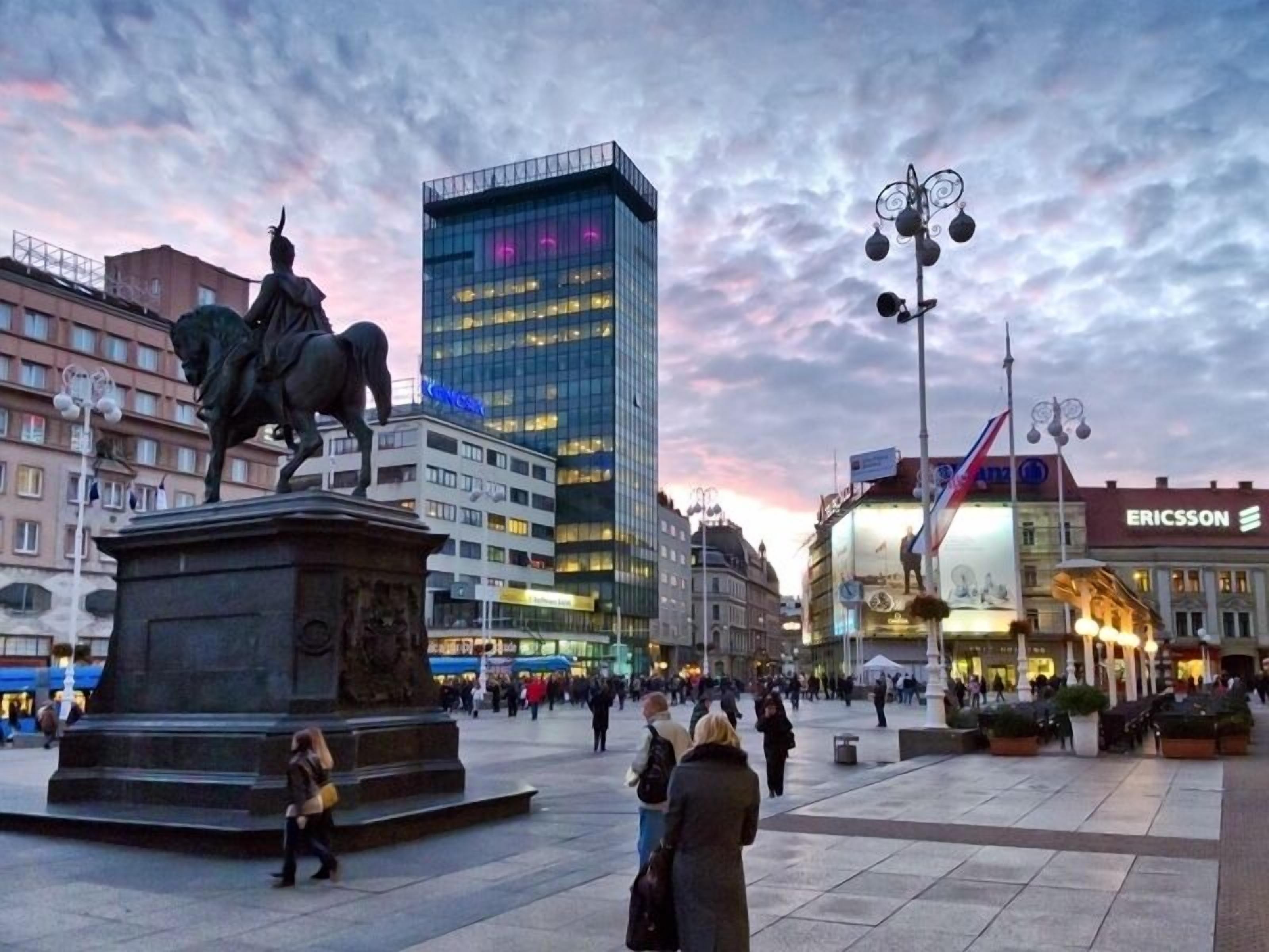 A public square with a statue, modern buildings, and a Ericsson sign.