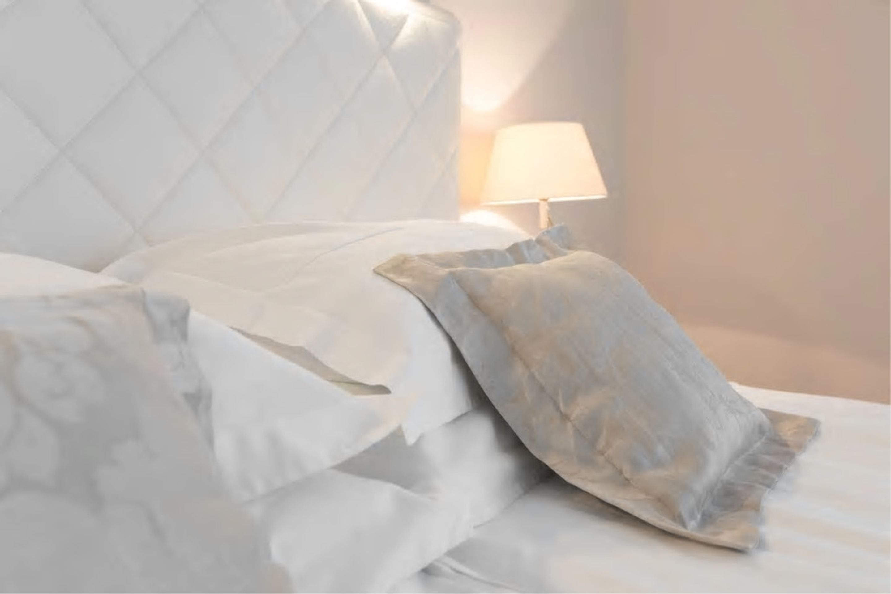 Una cama bien hecha con sábanas blancas y una sola almohada.