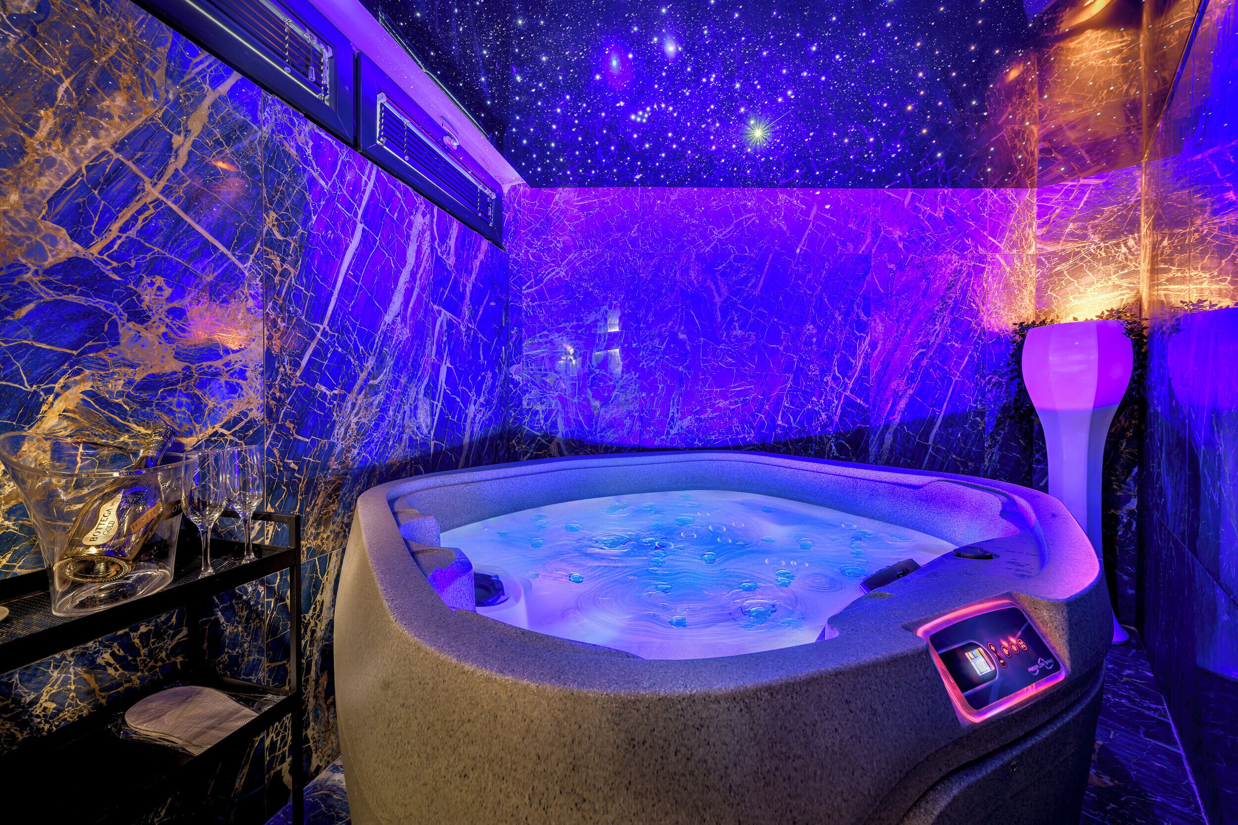 Un jacuzzi con panel de control digital, rodeado de paredes de mármol y un techo estrellado.