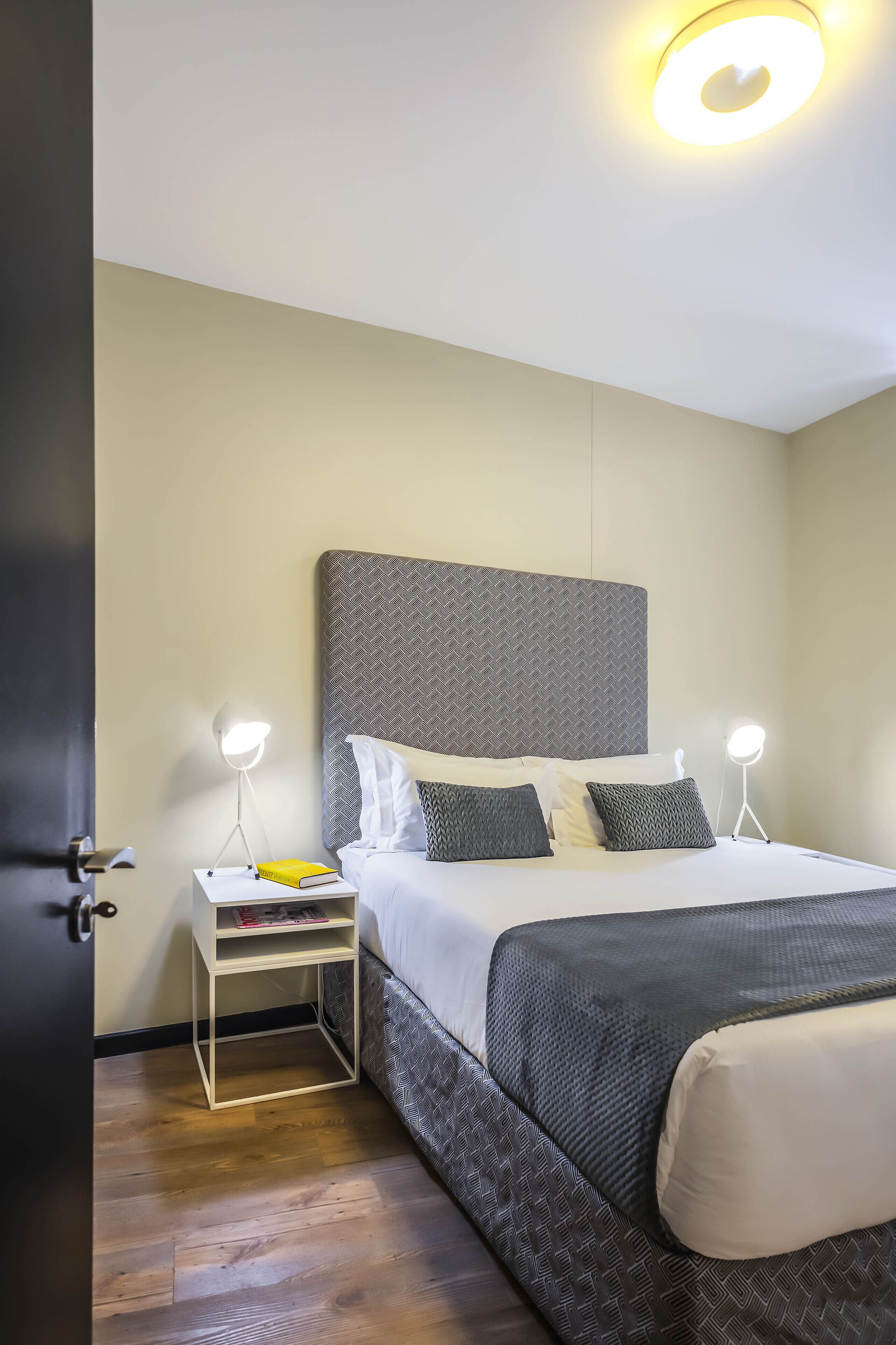 A neatly arranged hotel room with a bed, bedside tables, and a door.