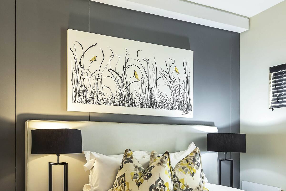 Een moderne slaapkamer met een groot bed, twee nachtkastjes met lampen, een plafondventilator en een kunstwerk aan de muur.
