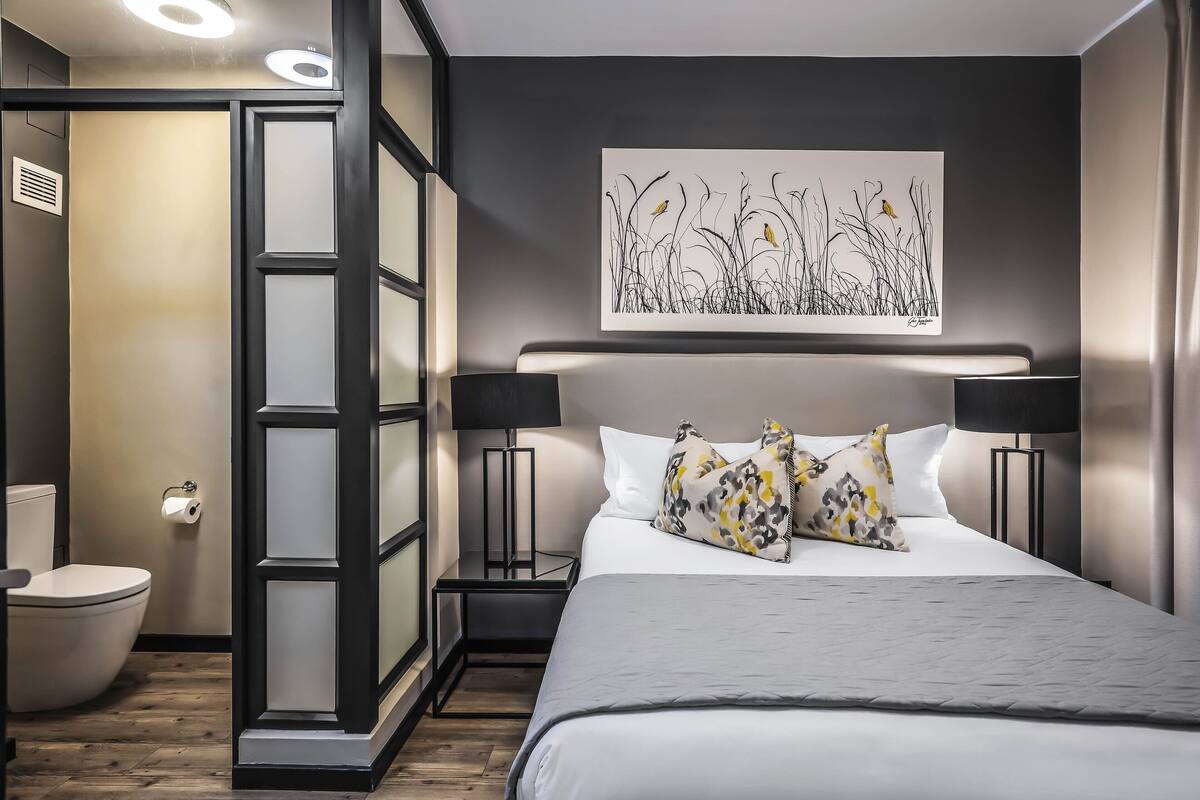 Een moderne slaapkamer met een groot bed, een nachtkastje, een wanddecoratie en een toilet.