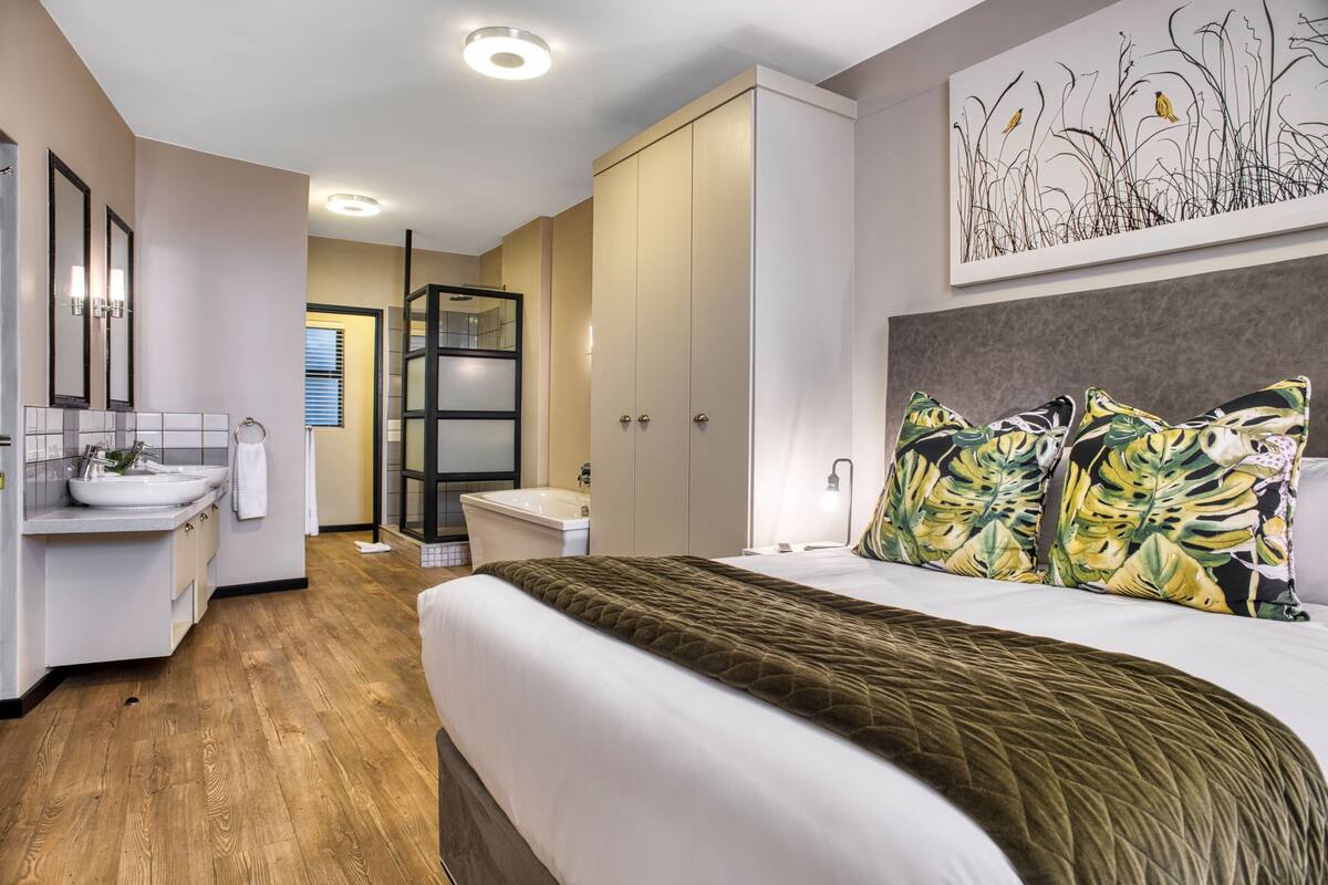 Een hotelkamer met een bed, een badkamer en een gang die naar een andere kamer leidt.