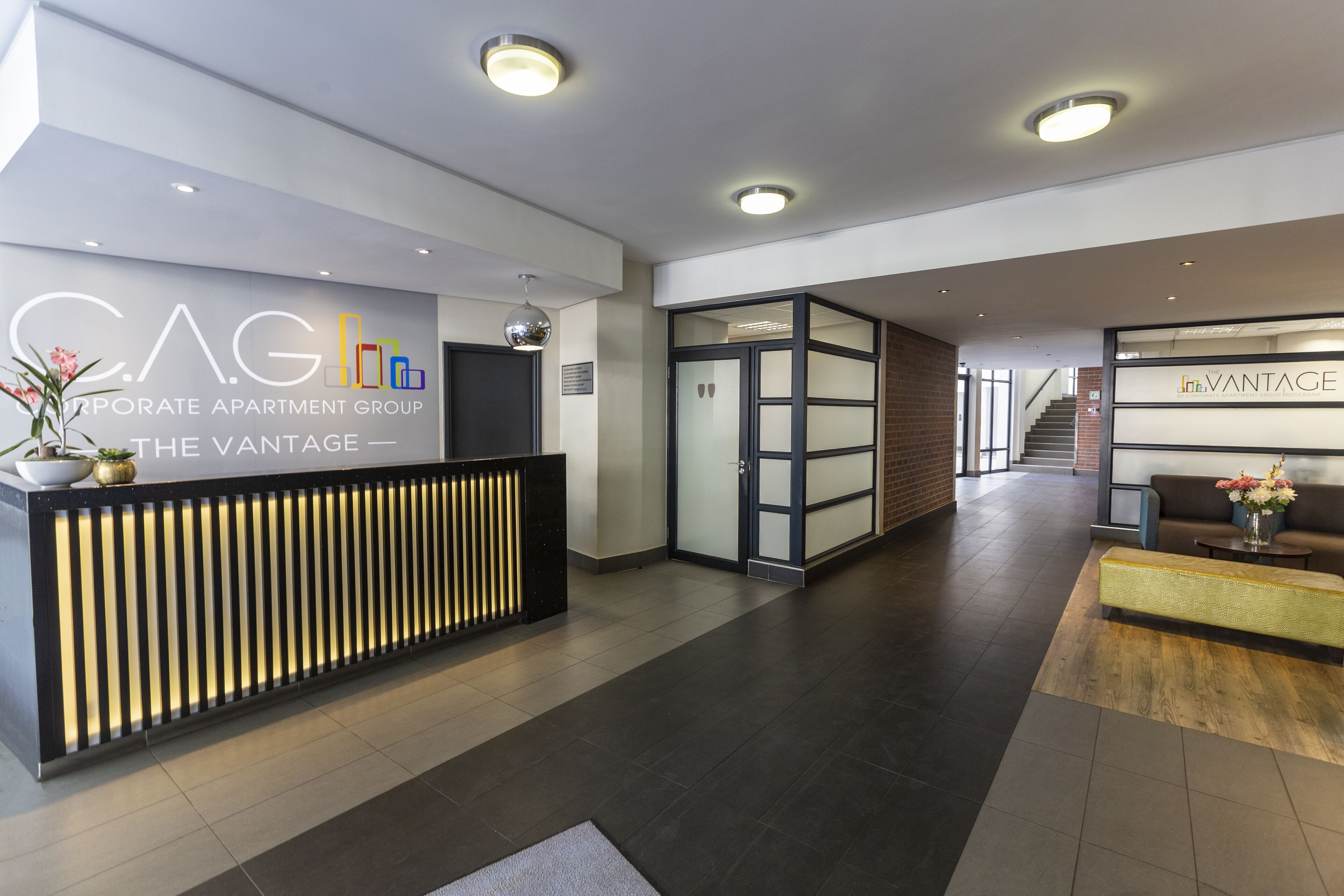 A modern reception area with a reception desk, a staircase, and a lounge area with a sofa and coffee table.