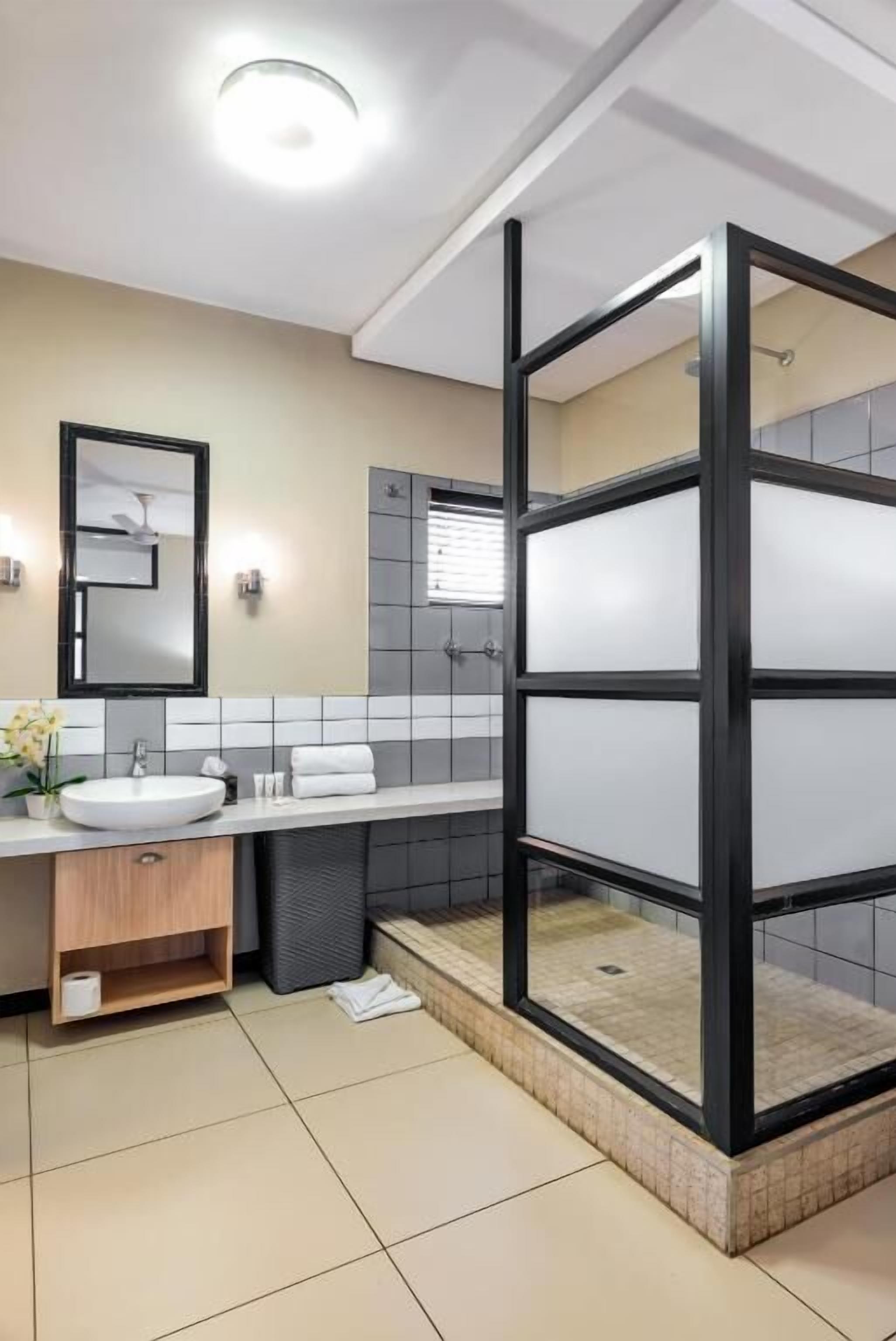 Un bagno moderno con box doccia in vetro, lavabo con specchio e schienale rivestito di piastrelle.