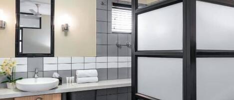 A modern bathroom with a glass shower enclosure, a sink with a mirror, and a tiled backsplash.