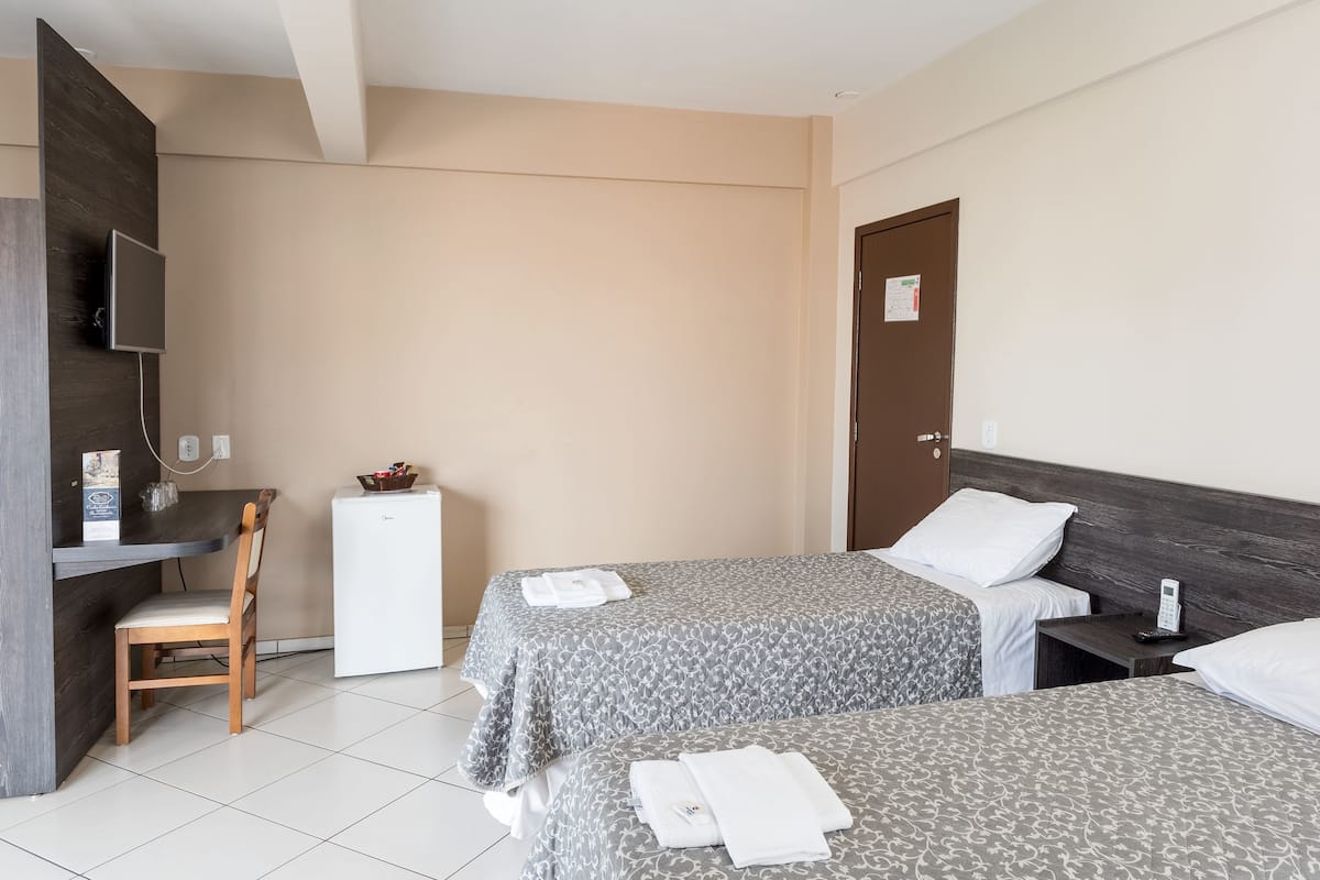 Ett hotellrum med två sängar, ett skrivbord, en stol, ett litet kylskåp och en tv.
