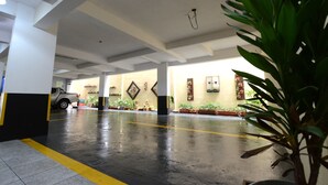 A covered parking area with a wet floor, potted plants, and a parked car. - Dom Sollievo Hotel (Telemaco Borba)