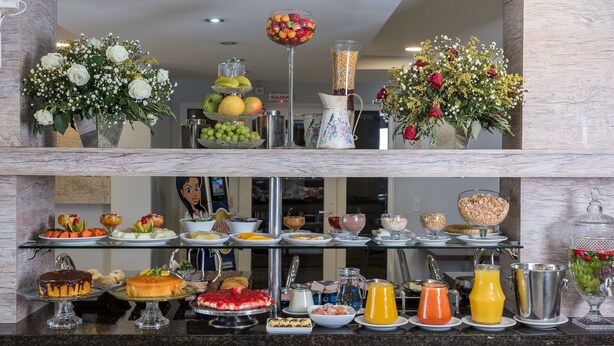 A buffet with various food items and drinks, including cakes, fruits, and beverages. - Dom Sollievo Hotel (Telemaco Borba)