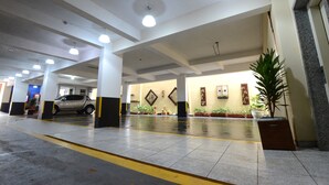 A spacious indoor area with a car parked under a covered section, potted plants, and a sign indicating an elevator. - Dom Sollievo Hotel (Telemaco Borba)
