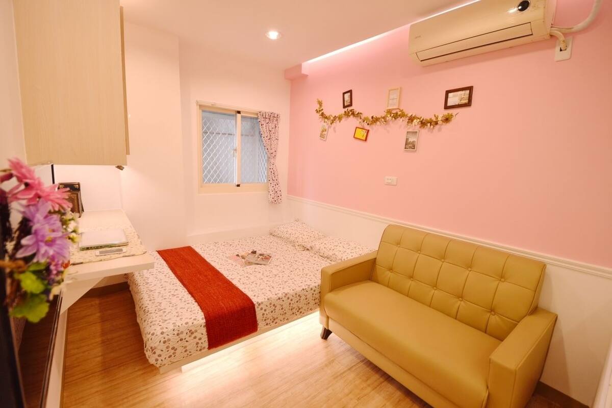 A small, cozy room with a bed, a sofa, a desk with a computer, and a window with curtains.