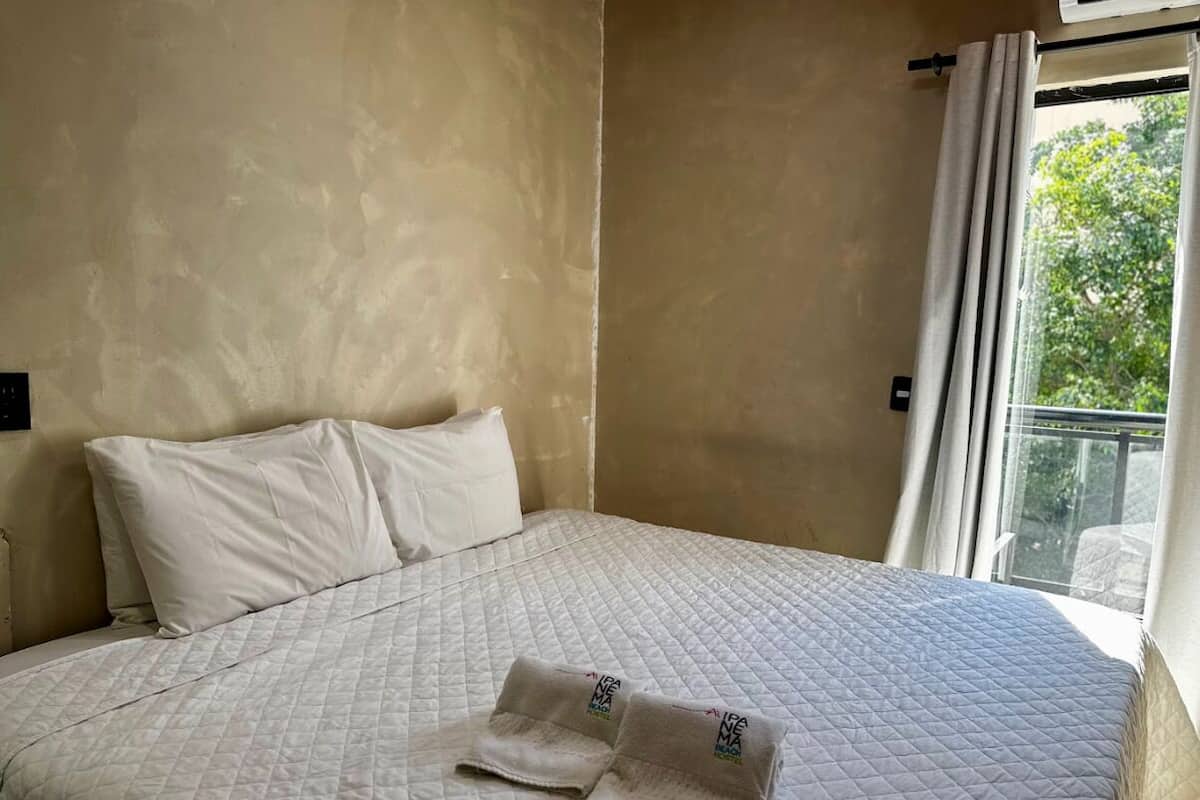 Una cama bien hecha con un edredón blanco acolchado y dos toallas dobladas encima.